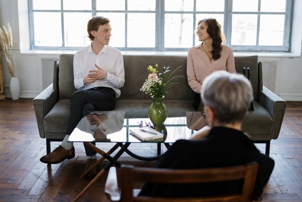 Sell Business A man and woman engage in a conversation on the couch discussing a lucrative exit plan for their health practice business. Exit Advisor Business Broker