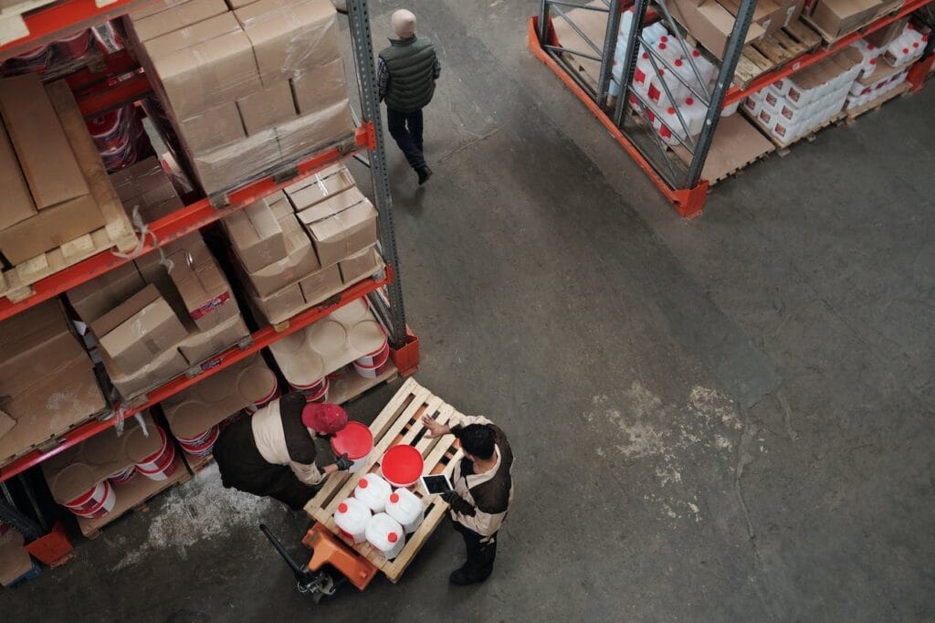 Sell Business A logistics business warehouse with two people working on a high-value pallet of boxes ready to sell. Exit Advisor Business Broker