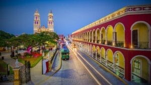 Benefits of Commercial Real Estate Investment in Mexico for Foreigners - Sell Business Evening view of a vibrant street in Mexico Real Estate, featuring colorful colonial buildings and the lit-up towers of a cathedral, with a horse-drawn carriage moving along the road. Exit Advisor Business Broker