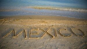 How to Handle Real Estate Disputes in Mexico as a Foreign Buyer - Sell Business The word "Mexico's Real Estate" is written in sand on a beach with gentle waves in the background. Exit Advisor Business Broker