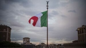 Investing in Mexico's Real Estate: Risks and Rewards for Foreigners - Sell Business Italian flag waving on a flagpole against a cloudy sky with historic buildings in the background, attracting foreign investors. Exit Advisor Business Broker