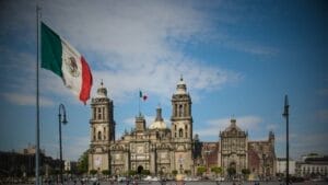 Ensuring Legal Compliance When Buying Business Property in Mexico - Sell Business A large Mexican flag waves in front of the Metropolitan Cathedral on a sunny day in Mexico City's Zócalo Square, attracting foreign investors interested in Mexico real estate. Exit Advisor Business Broker