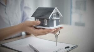 Tips for Successfully Selling Your Mexican Property as a Foreigner - Sell Business A person's hands holding a miniature house model and keys, with documents in the background on a desk, symbolizing investment opportunities for foreign investors in Mexico Real Estate. Exit Advisor Business Broker