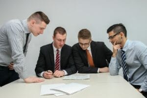 Turnaround Strategies for Distressed Firms - Sell Business Four business professionals discussing documents at a table in an office setting. Exit Advisor Business Broker