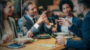 Effective Cash Flow Management in Declining Businesses - Sell Business Four professionals engaged in a lively discussion over market forecasting during a meal at a restaurant table. Exit Advisor Business Broker