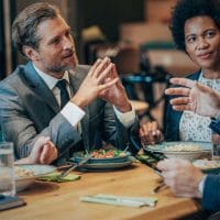 Effective Cash Flow Management in Declining Businesses - Sell Business Four professionals engaged in a lively discussion over market forecasting during a meal at a restaurant table. Exit Advisor Business Broker